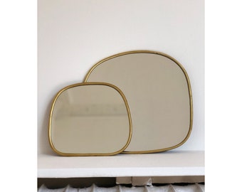 Peut inclure: Deux miroirs encadres dorés aux bords arrondis, l'un légèrement plus grand que l'autre, sont exposés sur une étagère blanche.