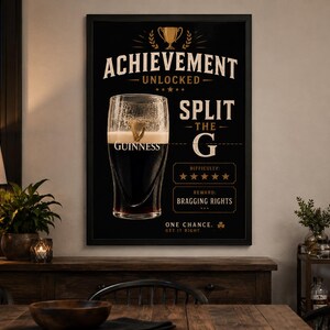 Puede incluir: P&oacute;ster de Guinness enmarcado en negro con el texto "ACHIEVEMENT UNLOCKED" y "SPLIT THE G". Una pinta de Guinness est&aacute; en el centro. El p&oacute;ster tambi&eacute;n incluye el texto "DIFFICULTY" y "REWARD BRAGGING RIGHTS".