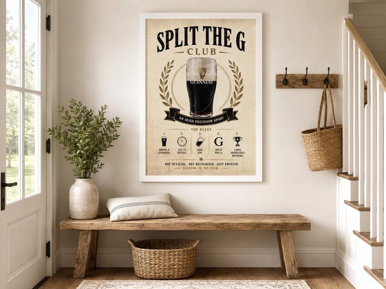 May include: A framed poster with the text "SPLIT THE G CLUB" and an illustration of a pint of Guinness. The poster is displayed above a wooden bench with a woven basket and a decorative pillow. A plant in a vase is also present.