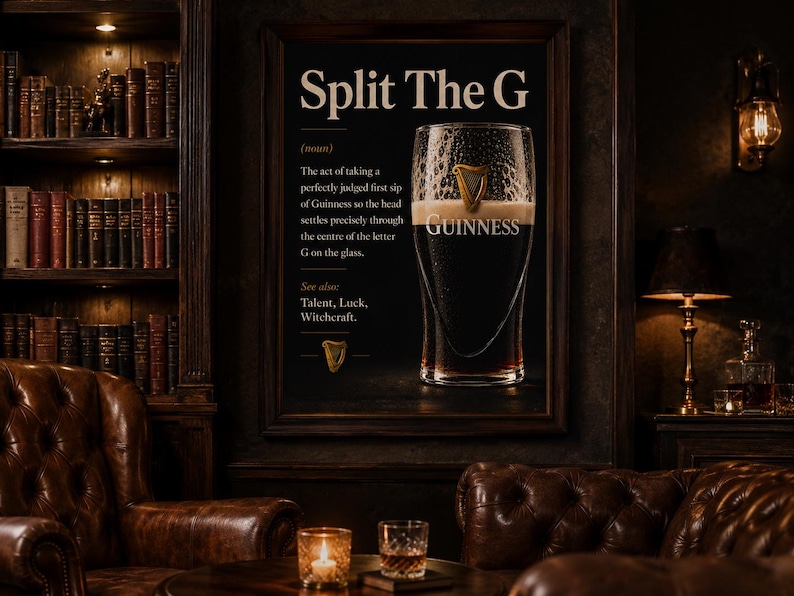 May include: A framed print with the text "Split The G" and a definition related to Guinness. The image features a pint of Guinness, a dark stout, with a creamy head. The setting is a dimly lit room with leather furniture and a bookshelf.