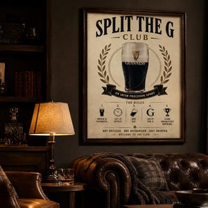 May include: A framed poster with the text "SPLIT THE G CLUB" and an illustration of a pint of Guinness. The poster includes the words "AN IRISH PRECISION SPORT" and "THE RULES". The poster is displayed in a room with a leather sofa and a wooden bookshelf.