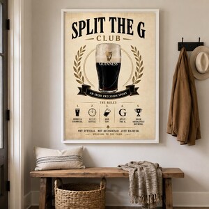 May include: A framed print with the text "SPLIT THE G CLUB" and an illustration of a Guinness pint. The print includes the rules of the club and is displayed above a wooden bench with a pillow and basket.