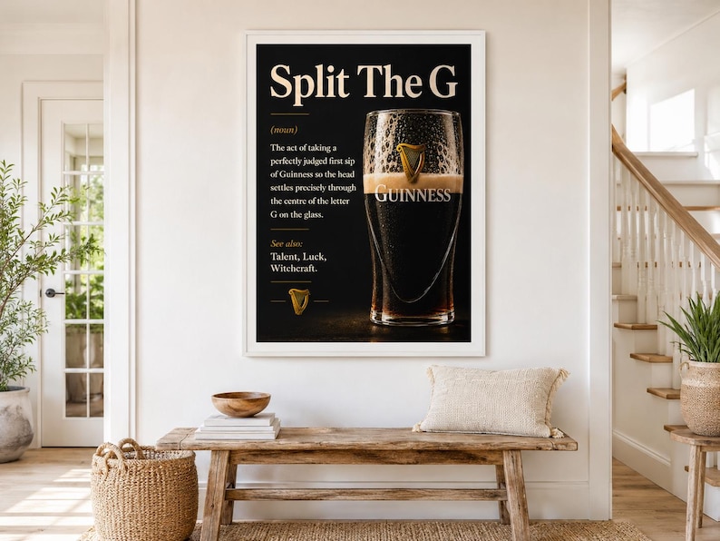 May include: A framed black and white print with the text "Split The G" and a definition of the act of drinking Guinness. The image features a pint of Guinness with the word "Guinness" visible. The print is displayed above a wooden bench.