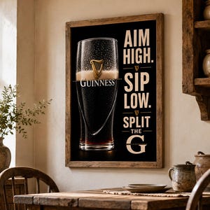 May include: A framed print featuring a pint of Guinness stout. The glass is filled with dark beer and a creamy head, with the Guinness logo visible. Text on the print reads "Aim High. Sip Low. Split the G."