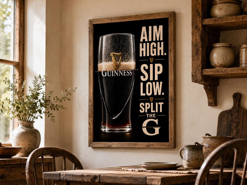 May include: A framed print featuring a pint of Guinness stout. The glass is filled with dark beer and a creamy head, with the Guinness logo visible. Text on the print reads "Aim High. Sip Low. Split the G."