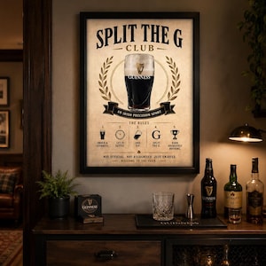 May include: A framed Guinness Club poster with a pint of Guinness in the center, surrounded by a laurel wreath. The poster includes the text "SPLIT THE G CLUB" and "AN IRISH PRECISION SPORT". A bar area with bottles and glassware is in the foreground.