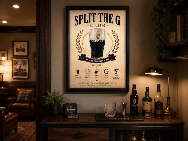 May include: A framed Guinness Club poster with a pint of Guinness in the center, surrounded by a laurel wreath. The poster includes the text "SPLIT THE G CLUB" and "AN IRISH PRECISION SPORT". A bar area with bottles and glassware is in the foreground.