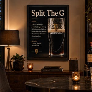 May include: A framed black and white print with the text "Split The G" and a definition of the perfect Guinness pour. The image includes a pint of Guinness and a gold harp symbol. The print is displayed in a room with a lamp and bar setup.