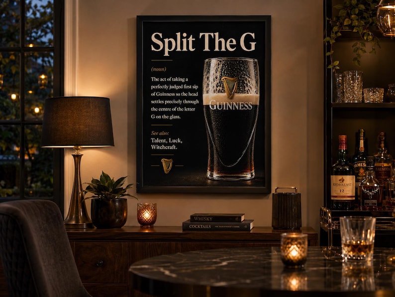 May include: A framed black and white print with the text "Split The G" and a definition of the perfect Guinness pour. The image includes a pint of Guinness and a gold harp symbol. The print is displayed in a room with a lamp and bar setup.