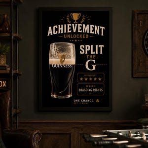 Puede incluir: Un p&oacute;ster negro enmarcado de Guinness con una pinta de cerveza negra. El p&oacute;ster dice "Achievement Unlocked" y "Split the G". La imagen tambi&eacute;n incluye un tablero de dardos, una estanter&iacute;a con una caja de Guinness y un letrero de "Game On".