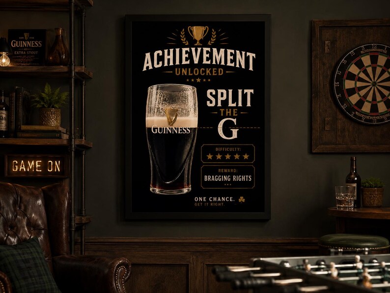 Puede incluir: Un p&oacute;ster negro enmarcado de Guinness con una pinta de cerveza negra. El p&oacute;ster dice "Achievement Unlocked" y "Split the G". La imagen tambi&eacute;n incluye un tablero de dardos, una estanter&iacute;a con una caja de Guinness y un letrero de "Game On".