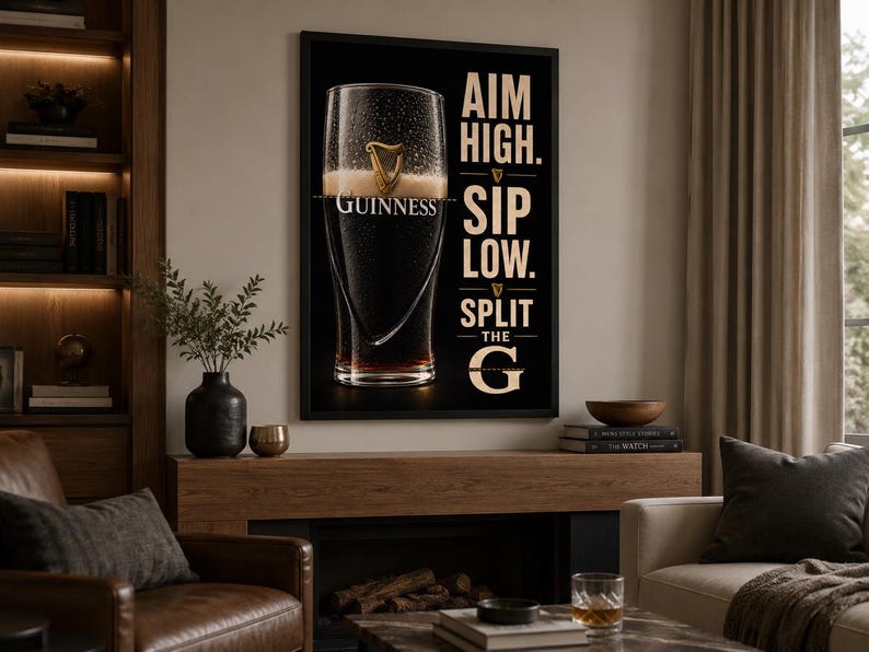 May include: A framed black and white Guinness advertisement. The image features a pint of Guinness with the text "AIM HIGH. SIP LOW. SPLIT THE G." The artwork is displayed in a living room setting with a fireplace and leather armchair.
