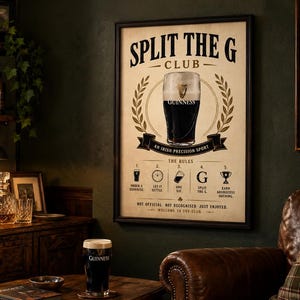 May include: A framed Guinness poster with a pint of Guinness in the center, surrounded by a laurel wreath. The poster reads "Split the G Club" and "An Irish Precision Sport." Below are the rules for enjoying Guinness. A pint of Guinness sits on a table.