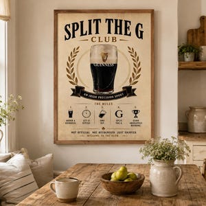 May include: A framed poster with the text "SPLIT THE G CLUB" and a Guinness glass illustration. The poster includes instructions and is displayed in a dining room setting with a wooden table and decorative elements.