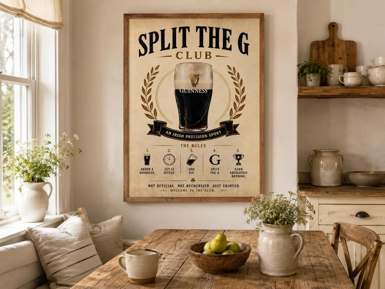 May include: A framed poster with the text "SPLIT THE G CLUB" and a Guinness glass illustration. The poster includes instructions and is displayed in a dining room setting with a wooden table and decorative elements.