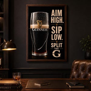 May include: A framed Guinness advertisement featuring a pint of stout with the brand's logo. The poster has the text "AIM HIGH. SIP LOW. SPLIT THE G" in a serif font. The image is set in a dark, classic study with a desk and leather chair.