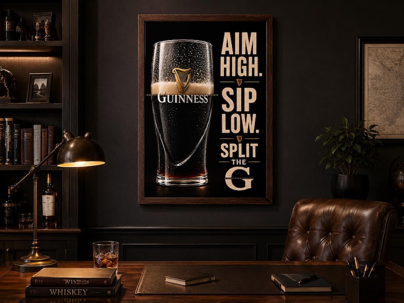 May include: A framed Guinness advertisement featuring a pint of stout with the brand's logo. The poster has the text "AIM HIGH. SIP LOW. SPLIT THE G" in a serif font. The image is set in a dark, classic study with a desk and leather chair.