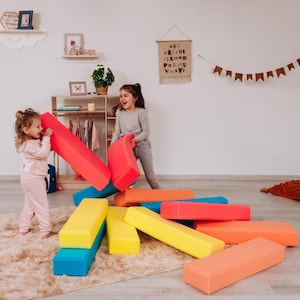 Peut inclure: Deux jeunes enfants jouent avec des blocs de mousse colorés. Les blocs sont de différentes formes et couleurs, notamment rouge, jaune, bleu et orange. Les enfants rient et semblent s'amuser avec cet équipement de jeu souple.