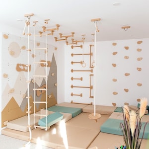 May include: A wooden indoor climbing gym set featuring a wall-mounted climbing board with mountain graphics, a rope ladder, horizontal bars, gymnastic rings, and a wooden swing, all arranged over soft beige and light green floor mats.