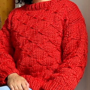 May include: A red knitted sweater with a unique bow pattern. The sweater has long sleeves and a crew neck.