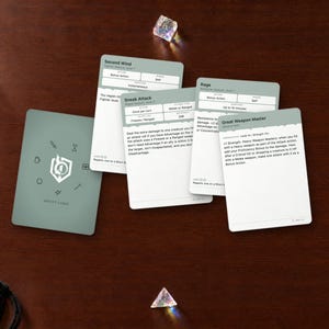 May include: A set of sage green and white tabletop role-playing game ability cards featuring text for Second Wind, Sneak Attack, Rage, and Great Weapon Master, accompanied by a gold pen and three translucent polyhedral dice.