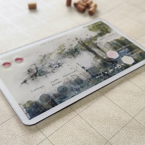 Könnte beinhalten: Eine weiße Plastikkarte mit einem Aquarellhintergrund und schwarzem Text. Der Text lautet "Spells Known", "Hemocraft Die", "Cantrips" und "Prof + Str + 8".