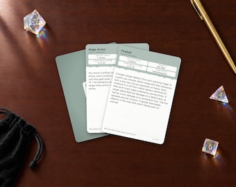 May include: Two rectangular game cards with light green backs and white fronts featuring the text Mage Armor and Fireball. The cards are surrounded by a black drawstring pouch, a gold pen, and three translucent polyhedral dice.