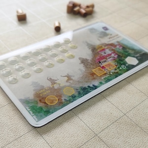 Può includere: Un tabellone di gioco in plastica trasparente con un design ad acquerello di un villaggio giapponese. Il tabellone è composto da una griglia di 36 piccoli cerchi e da un bordo bianco. Il testo sul tabellone recita "Total Ki Points" e "Prof.  +  Vice  +  8".