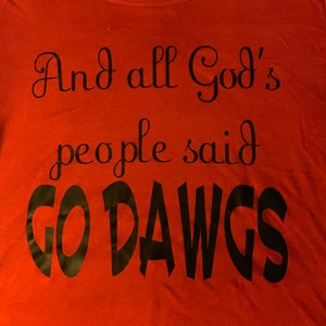 May include: Red t-shirt with the text "And all God's people said GO DAWGS" in black script. The shirt has a scoop neck and a tag that says "TIME AND TRU".