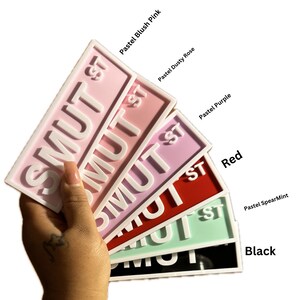 May include: A set of six "SMUT ST" signs in various colors, including pastel blush pink, dusty rose, purple, red, pastel spearmint, and black.