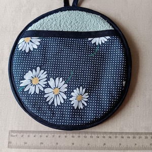May include: A round blue and white pot holder with a daisy print and white polka dots. The pot holder has a light blue terry cloth pocket and a black loop for hanging.