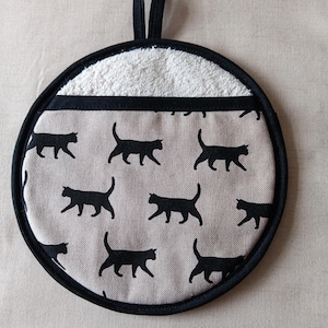 May include: Round black and white pot holder with a black cat pattern and a white terry cloth lining. The pot holder has a black loop handle.