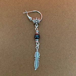 May include: A silver hoop earring with a black bead and a silver feather charm.