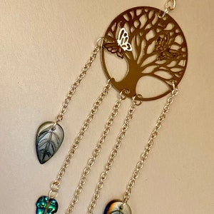 May include: A gold metal tree of life wind chime with five iridescent glass leaves hanging from it. The leaves are in shades of green, blue, and white.