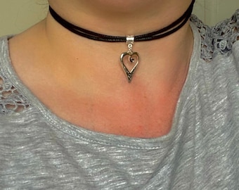 May include: A silver heart pendant necklace with a black leather choker. The heart pendant has a swirl design and a small clear stone in the center.