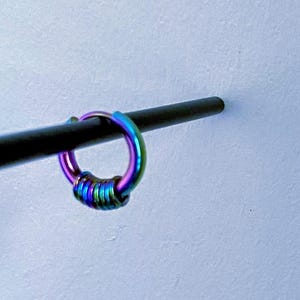 May include: A rainbow coloured metal hoop earring with a twisted design.
