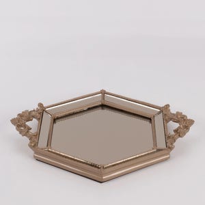 May include: A decorative tray with a mirrored surface and a gold-colored frame. The tray has a unique geometric shape with ornate handles on each side. The tray is designed to hold items and add a touch of elegance to any space.