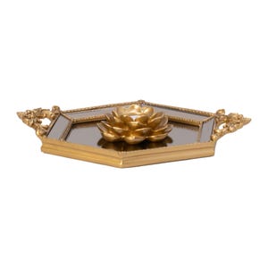 May include: A hexagonal gold-toned tray with a mirrored base and ornate handles on each side. Centered on the mirror is a three-dimensional gold-toned lotus flower sculpture. The frame features intricate detailing along the edges.