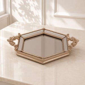 May include: A hexagonal mirrored tray with a metallic gold-toned frame. The tray features a central hexagonal mirror panel surrounded by six smaller mirrored sections, all enclosed by a decorative, ornate border with two sculpted side handles.