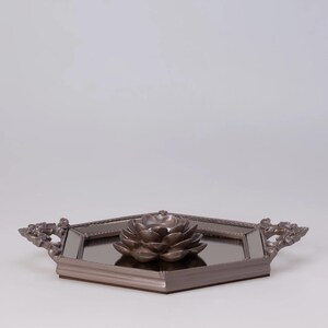 May include: A decorative tray with a mirrored surface and a bronze-colored lotus flower candle holder. The tray has ornate handles and a geometric shape, perfect for home decor.