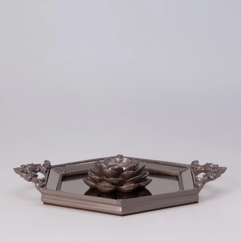 May include: A decorative tray with a mirrored surface and a bronze-colored lotus flower candle holder. The tray has ornate handles and a geometric shape, perfect for home decor.