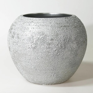 Könnte beinhalten: Eine silberfarbene, kugelförmige Vase mit strukturierter Oberfläche. Die Vase hat eine weite Öffnung und einen dunkelgrauen Innenraum. Die Außenseite hat ein raues, körniges Aussehen, das ihr einen einzigartigen, modernen Look verleiht. Die Vase eignet sich für dekorative Zwecke.