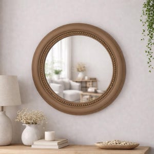 Pode incluir: Um espelho de parede circular com uma moldura larga em castanho mate e uma borda interior decorativa com contas. A superf&iacute;cie do espelho reflete um espa&ccedil;o interior luminoso, destacando o vidro claro e o acabamento liso da moldura redonda.