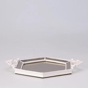 May include: A white, octagonal mirrored tray with ornate, floral-style handles. The tray has a mirrored surface and a white frame with a decorative trim. The base is a dark brown color.