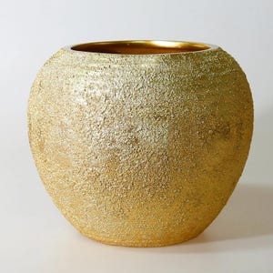 May include: A round, gold-colored vase with a textured surface. The vase has a wide opening and a smooth, gold-colored interior. The exterior has a rough, granular texture, giving it a unique, decorative appearance. The vase is likely used for home decor.