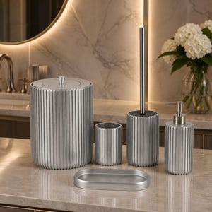 Peut inclure: Un ensemble d'accessoires de salle de bain en cinq pièces avec une finition argent brossé et une texture nervurée verticale. Le set comprend une poubelle à couvercle, un porte-brosse à dents, une brosse WC, un distributeur de savon et un plateau ovale.