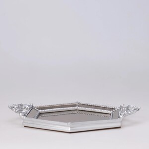 May include: A silver-colored, geometric tray with a mirrored surface. The tray has decorative handles on each side and a brown base. The tray is designed with a modern aesthetic.