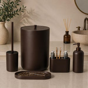 May include: A set of dark brown bathroom accessories. The set includes a toilet brush, a bin, a toothbrush holder with toothbrushes, a soap dispenser, and a small oval tray with jewelry.