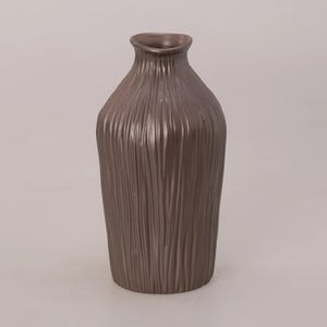 Könnte beinhalten: Eine hohe, braune Vase mit einer strukturierten, vertikal gestreiften Oberfläche. Die Vase hat einen schmalen Hals und einen breiteren Körper, geeignet für die Präsentation von Blumen oder als dekoratives Element. Die Vase besteht aus Keramik oder einem ähnlichen Material.