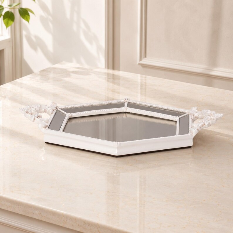May include: A hexagonal mirrored tray featuring a white frame with beaded detailing along the edges. The tray includes two ornate, decorative handles on opposite sides, providing a reflective surface within the white border structure.